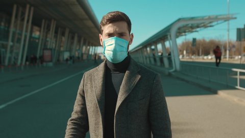 COVID-19 coronavirus infection man wearing Protective Face Mask near airport look at camera serious pandemic disease virus male tourist epidemic air health illness slow motion