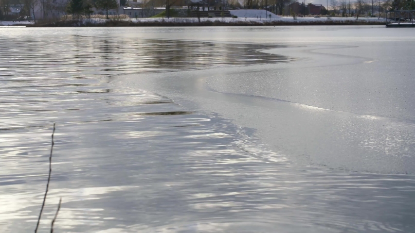 Sheet of ice melting on partly frozen city lake, static medium shot