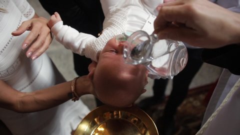 Christening ceremony in church with infant. The priest pours water on the child when his parents hold him.