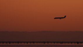 Short video clip of an aircraft as it flies down for a landing; orange skies in the background with mountain silhouettes during sunset.