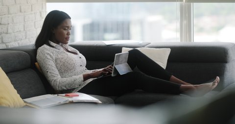Black woman working from home during quarantine. African american people and mobile work, doing telework. Young businesswoman at work with laptop computer, lying on sofa. Remote work from home office