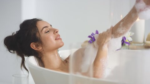 Closeup smiling woman washing hands with foam in slow motion. Relaxed girl resting in bath with bubbles at luxury hotel. Sexy woman relaxing bath at home.
