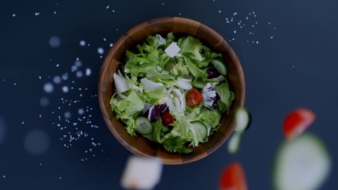 OVERHEAD FLAT LAY Sliced tomatoes, cucumbers, salt and cheese falling into salad plate. Healthy food concept. 300 FPS Slow motion