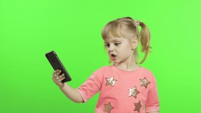 Little girl using smartphone. Portrait of child in pink blouse with smartphone making photos and selfies. Kid enthusiastically play with mobile phone. Green Chroma Key background for keying