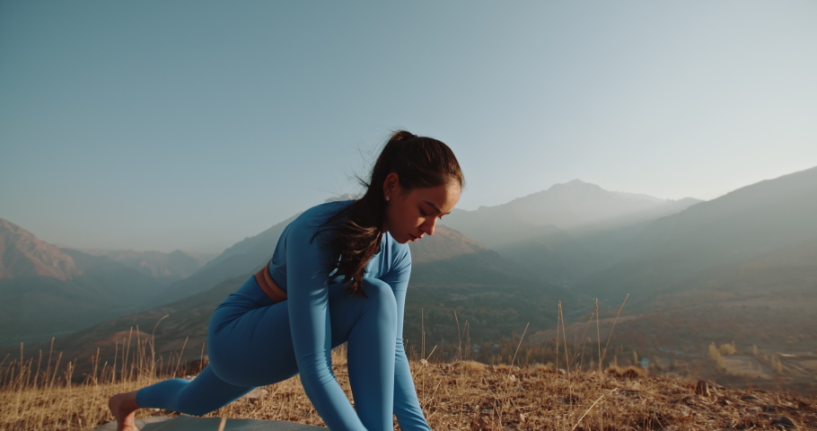 Yoga session in mountains. Young athletic girl training in cliffy mountains during sunrise, doing various yoga poses - healthy lifestyle concept 4k footage Royalty-Free Stock Footage #1048524274