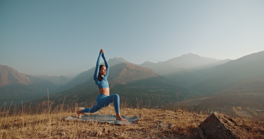 Yoga session in mountains. Young athletic girl training in cliffy mountains during sunrise, doing various yoga poses - healthy lifestyle concept 4k footage