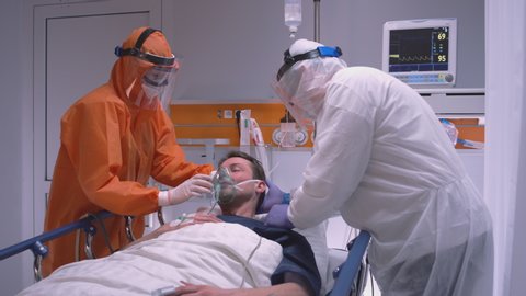 Doctor in Protective Suit Putting on Oxygen Mask on Patient Suffering from Coronavirus - Wide Dolly Shot in Slow Motion