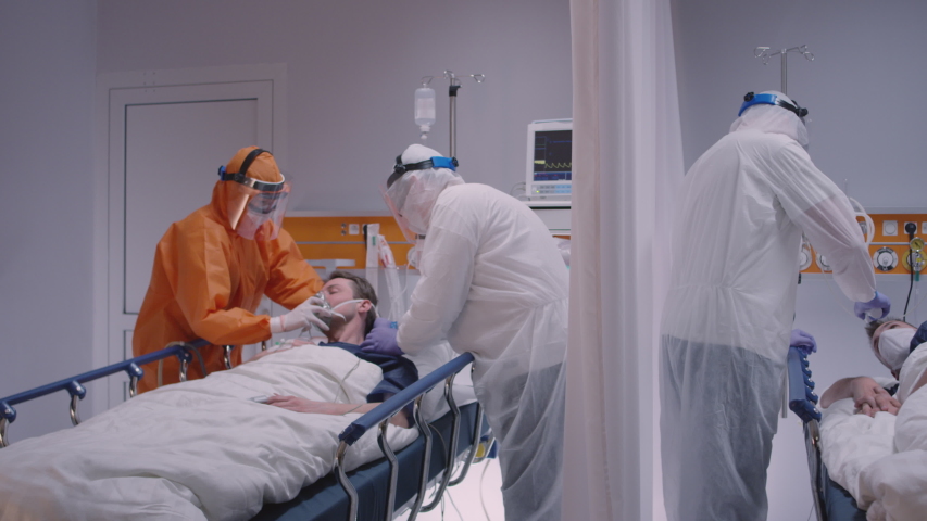 Doctor in Protective Suit Putting on Oxygen Mask on Patient Suffering from Coronavirus - Wide Dolly Shot in Slow Motion Royalty-Free Stock Footage #1048526962