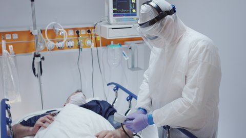 Doctor in Protective Suit Measuring Coronavirus Patient's Blood Pressure - Wide Shot