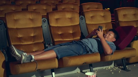 A boy laying down and playing a game and take a photo in the cinema