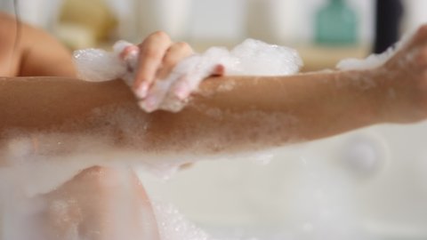 Close up unrecognized woman washing body with foam at home bath. Sexy woman hands touching skin in bathtub in slow motion. Closeup attractive girl cleaning skin in bathroom.