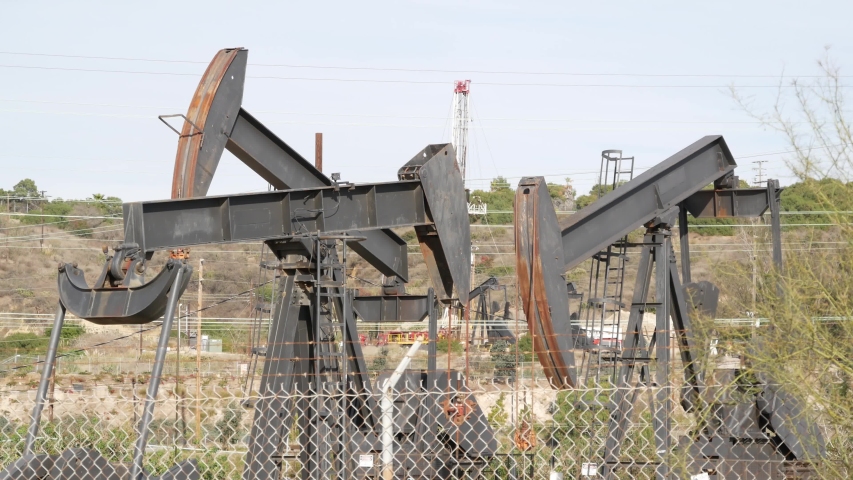 Industrial urban landscape. La Brea Inglewood in Los Angeles. Well pump jack operating behind the fence. Drilling rig extract crude oil. Oil mining machine with working piston. Oil and gas industry.