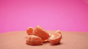 Ripe peeled mandarin, rotate on pink and old paper background 4k video with color correction