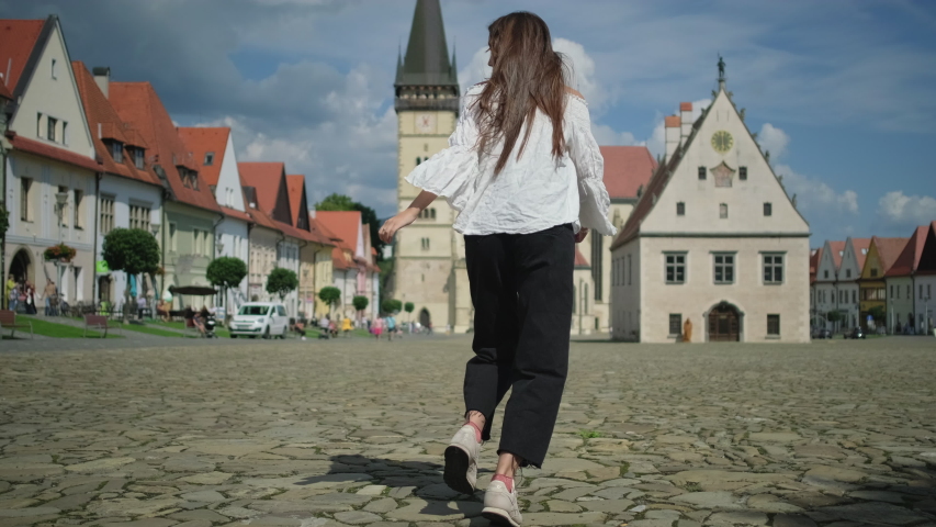 Slow motion shot of girl at Town Hall Square in Bardejov, Slovakia. She running and turning to the camera with happy look