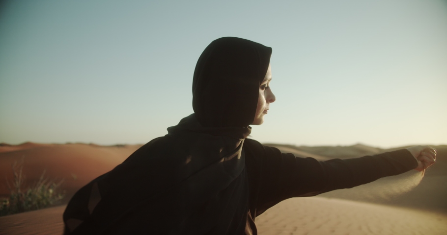 Arab woman in hijab and abaya in the desert at sunset holds sand in her hands. 4K Slow Motion Royalty-Free Stock Footage #1048546804