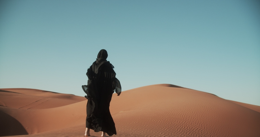 Young beautiful girl in traditional Abaya dress walks along the dunes in the desert of Dubai. 4K Slow Motion