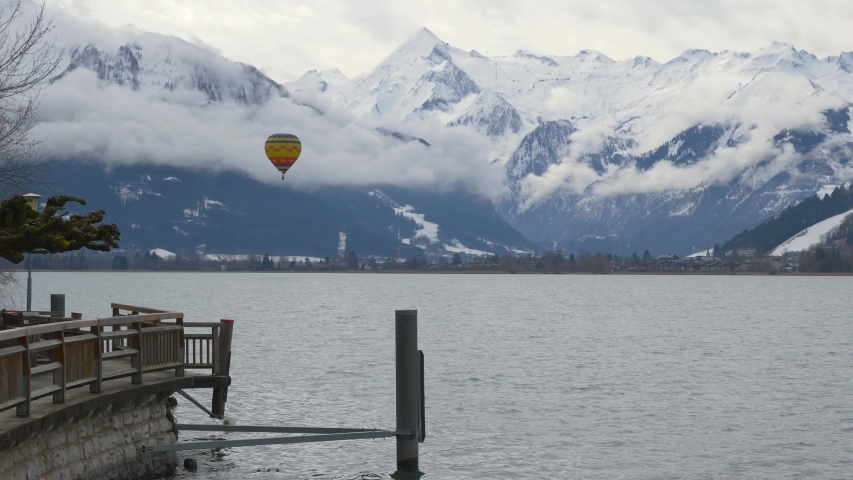 single hot air ballon aerostat flying over mountain lake Zell, zell-am-see, with snowy alps mountains