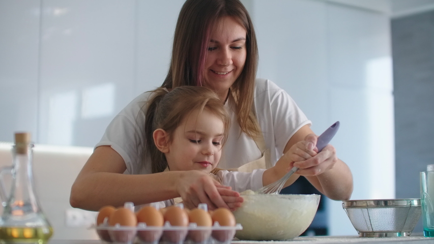 Caucasian mother and daughter having fun while making dough on kitchen. Happy family in the kitchen. Child daughter preparing the dough, bake cookies. Royalty-Free Stock Footage #1048554562