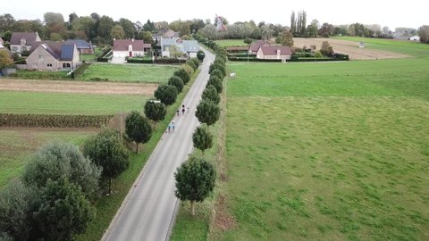 aerial drone shot of cyclists driving on a road in the countryside, near a village. bicyclist
driving in a street away from a village into the countryside, Belgium, Europe.