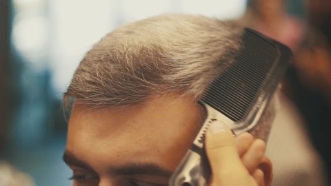 Close up of Hairdresser makes the cut. Fashionable haircut. Barber cuts hair of a man with razor, brush. Hipster lifestyle. Professional stylist. Portrat view. Man model. Barbershop. Modern Hairstyle