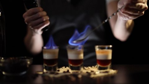 Bartender setting B-52 cocktail on fire using a culinary torch and burning some brandy on a cocktail spoon