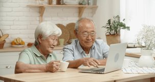 Closeup shot of senior asian couple using a computer, sitting in kitchen and doing online shopping or having a video chat and talking - happy pension and retirement concept 4k footage