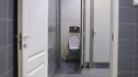 A woman with urinary incontinence in public restroom runs in toilet cabin. Finally a woman going out from cabin
