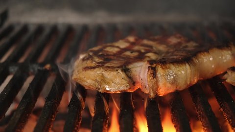 Slide motion shot of cooking barbecue steak meat on grill. Roast pork tenderloin on an open fire BBQ. Close- up of grilled steak with fire and smoke on brazier.