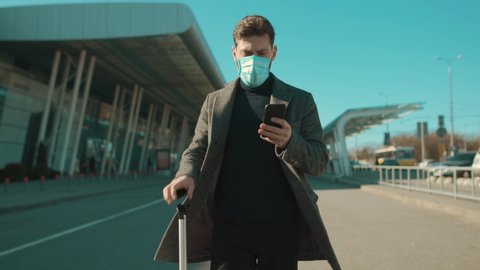 Close up man wearing Protective Face Mask use phone coughs hold suitcase COVID-19 coronavirus infection near airport pandemic disease virus male tourist epidemic air health illness slow motion