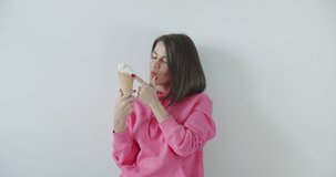 Young woman eating ice cream over white wall background. Girl enjoying sweet yummy. 4k raw video footage slow motion