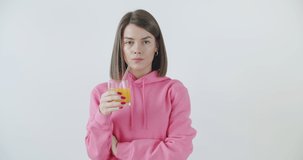 Caucasian young girl in stylish outfit drinking juice with glass straw and smiling over white wall background. Zero waste healthy concept. 4k raw video footage slow motion