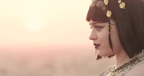 close up girl looks like the queen of cleopatra. the girl's eyes are raised with arrows, dark lipstick on her lips. sunset.