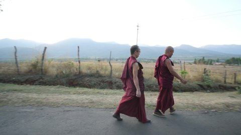 Kollegal, Karnataka / India - March 14 2020: Wide angle panning shot of two monks walking on an empty road with beautiful mountains in the background during evening