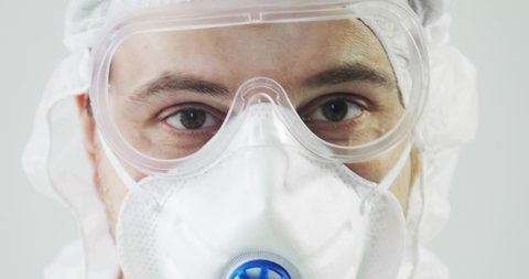 Human man doctor in protective clothes during coronavirus pandemic, portrait. Part of face in suit, mask and glasses on white background in clinic or hospital. Protection from epidemic concept.