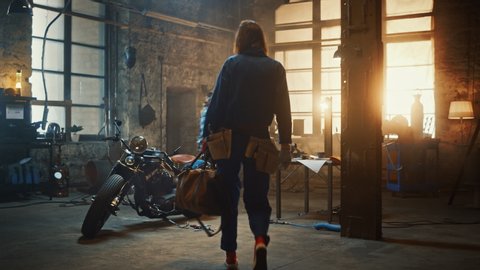 Young Beautiful Female Mechanic Comes to Garage and Starts Working on a Custom Motorcycle. Talented Girl Wearing a Blue Jumpsuit. She Uses a Spanner to Tighten Nut Bolts. Creative Authentic Workshop.