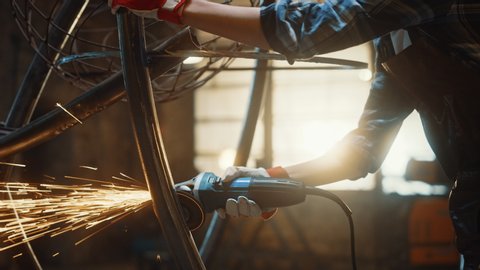 Close Up of Hands of a Metal Fabricator Wearing Safety Gloves and Grinding a Steel Tube Sculpture with an Angle Grinder in a Studio. Working with a Handheld Power Tool in a Workshop.