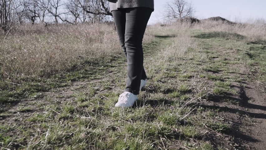 A woman in sports shoes walks along a rough forest road.
