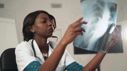Scientist, Microbiologist or Doctor, black woman checking examining viral infection or pneumonia lesion on Chest X-ray film in laboratory for analysis and sampling of Coronavirus 2019, COVID-19