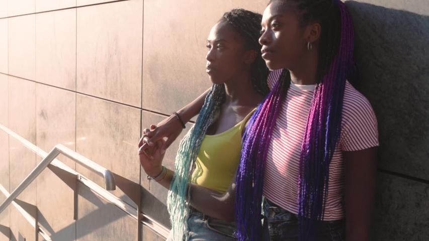 Two young beautiful black sisters outdoor posing looking over - supportive, objective, contemplation concept