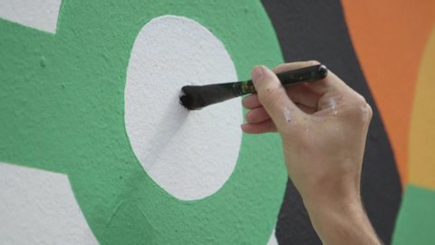 Close-up Off Man Painting A Black Dot Withing A Green Circle On A Street Wall