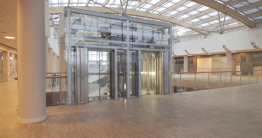 Interior of modern empty shopping mall with elevator. Abstract ceiling and escalator in hall of shopping mall. Empty hallway with elevator and abstract ceiling in modern shopping mall