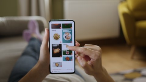 Orders Pizza Using Online Delivery. Woman Orders Food Home In Online Store Using a Smartphone. Female Ordering pizza using food delivery app. Screen is blurred. Focus on hand.