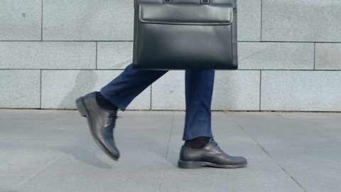 Side view unrecognizable businessman legs walking on city street. Close up male worker with briefcase going for work outdoors in slow motion. Business man in leather shoes walking on sidewalk