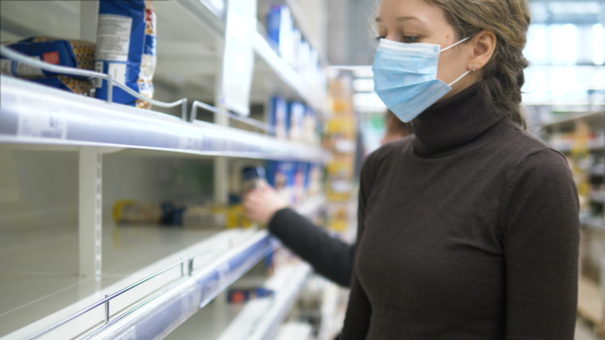 A woman in a medical mask takes the last bag of food in the supermarket. Empty store shelves due to pandemic panic