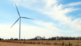 Single windmill against blue sky is seen from pov of a moving car in this hand held slow motion clip.