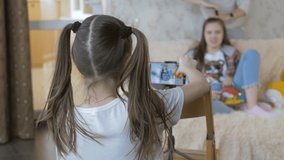 The girl 8-year-old shooting video her sister teen on a smartphone. The girl teenager sitting on the couch and leadership blog.