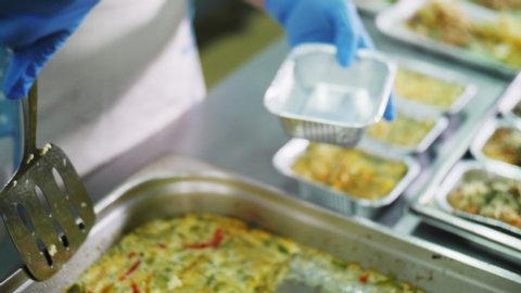 barmaid in rubber gloves puts piece of baked omelet with vegetables into foil container in canteen close view