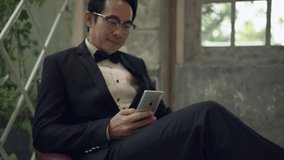 Asian groom sitting on a red chair using smartphone are smiling and happy in studio. Handheld shot. Real life	 - Powered by Shutterstock - Get 15% off with code: PIKWIZARD15
