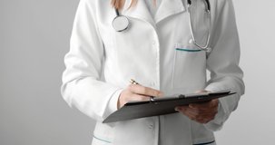 Close up of medical worker in white lab coat standing in studio with white background and writing in clipboard. Close up of female doctor filling out prescription