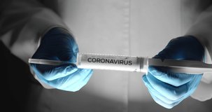 Medical specialist in lab coat and protective gloves holding white syringe with name of coronavirus, close up. Concept of pandemic and vaccination